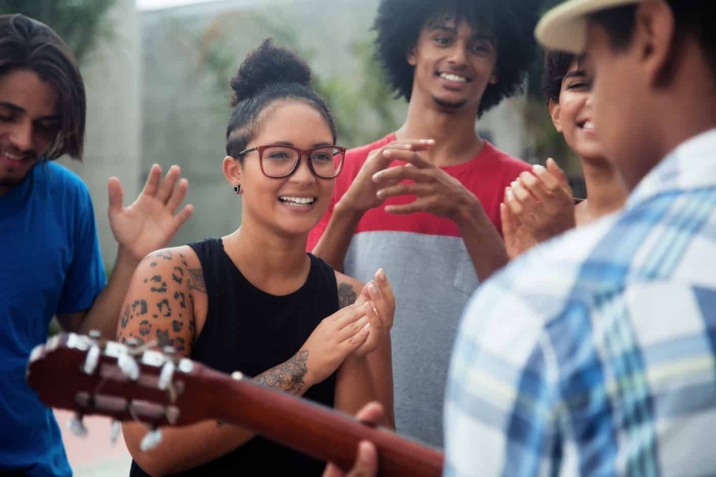 Teens clapping, smiling, and listening to guitar music.