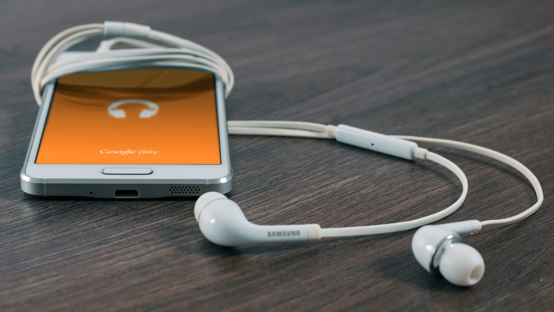 a Samsung smartphone wrapped in its earbuds on a wood surface