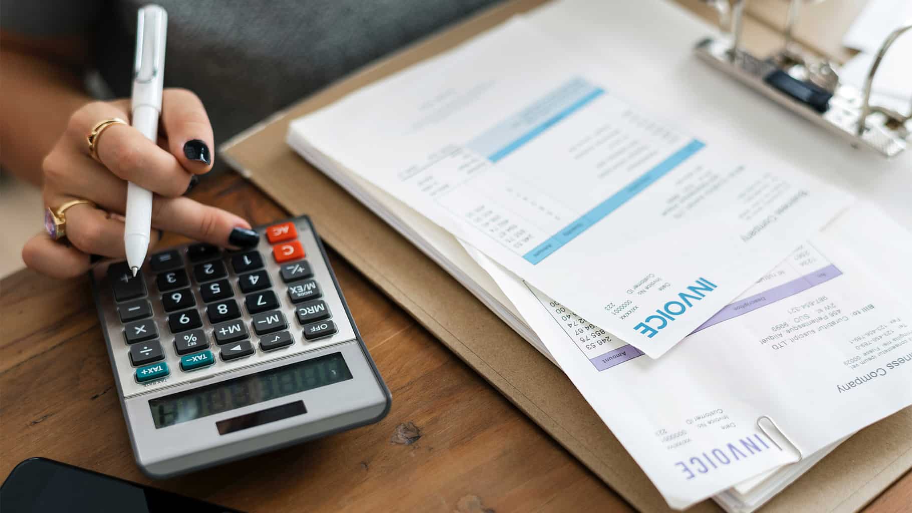 closeup of a hand using a calculator and a set of invoices in a notebook