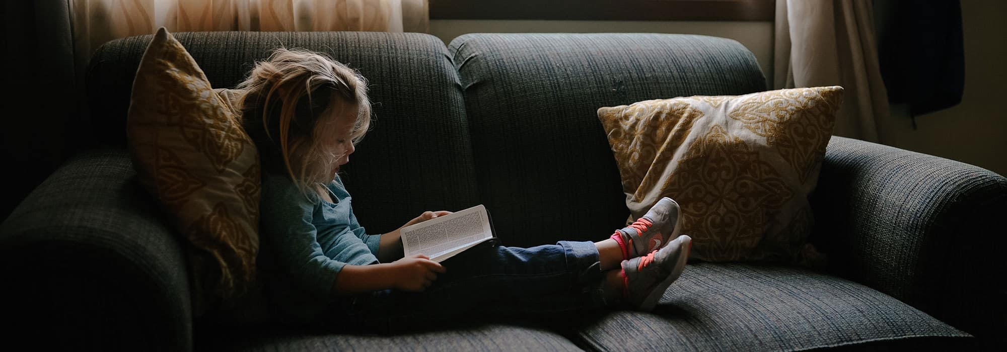 a girl reading a book on a sunlit couch