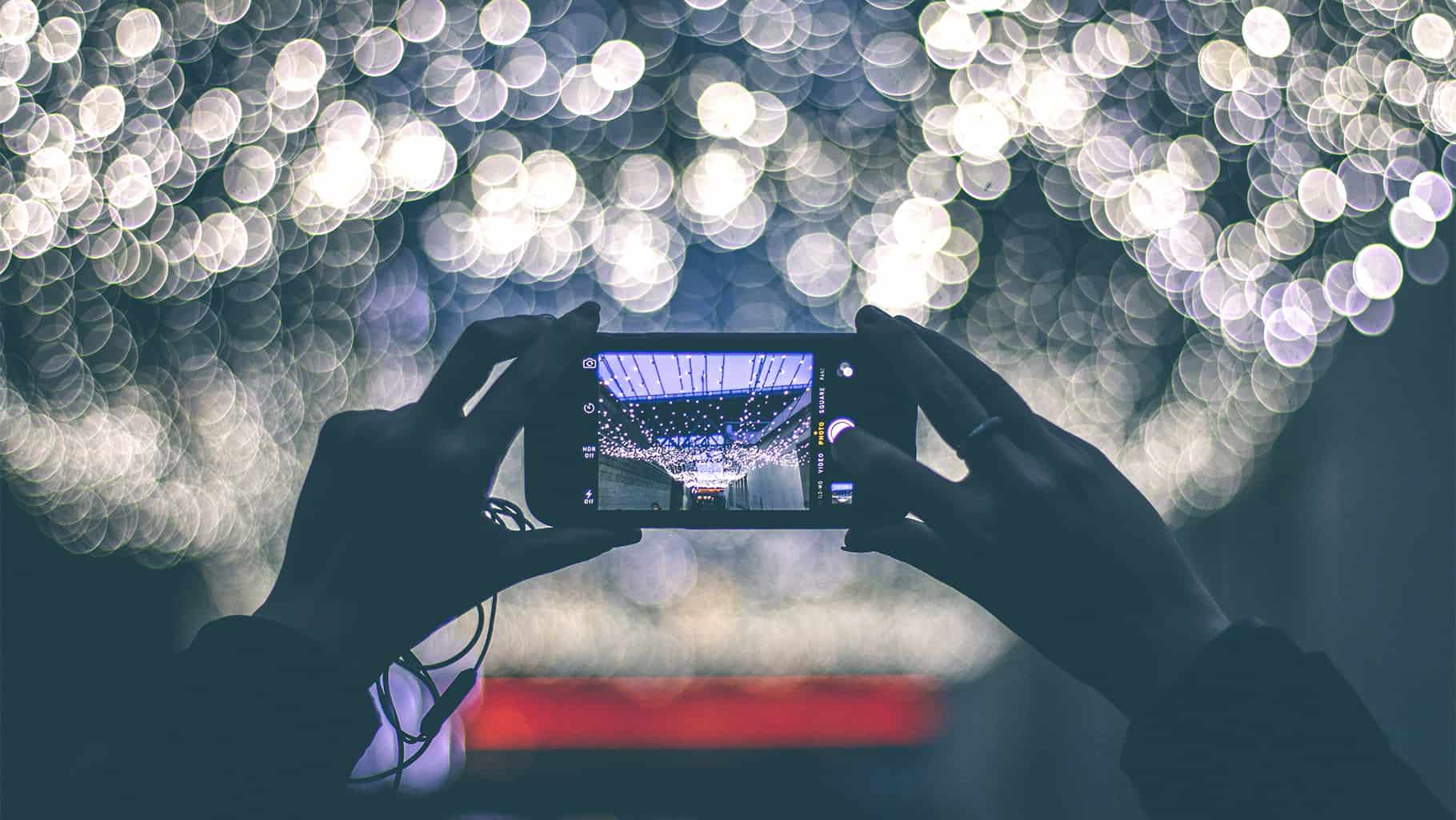 hands holding a smartphone taking a picture of string lights