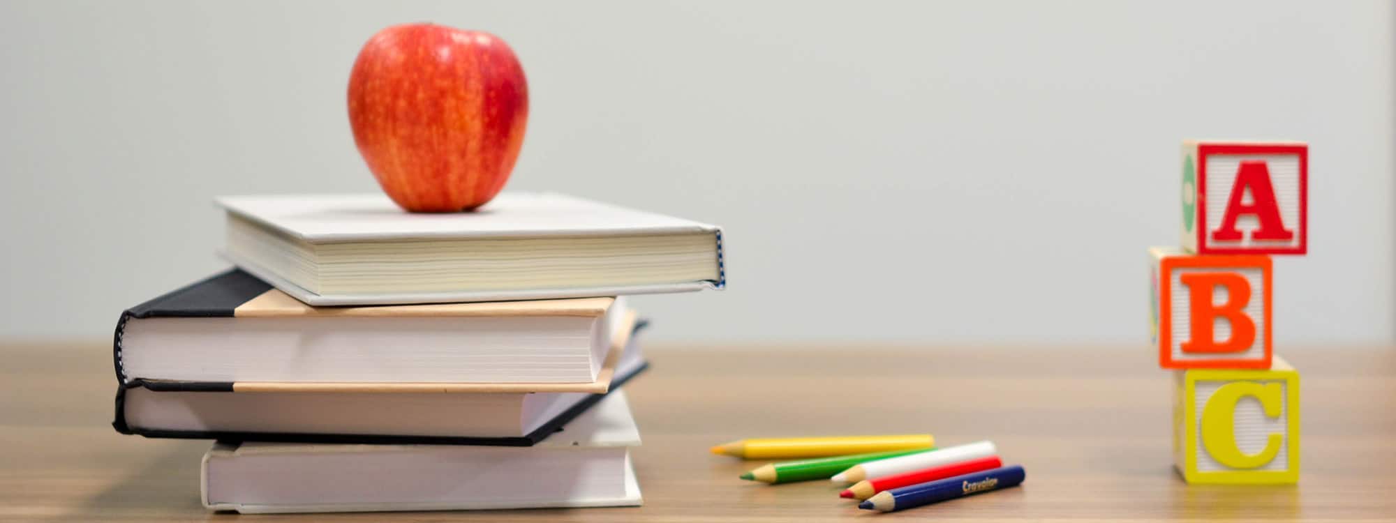 an apple on a stack of books with letter blocks and colored pencils