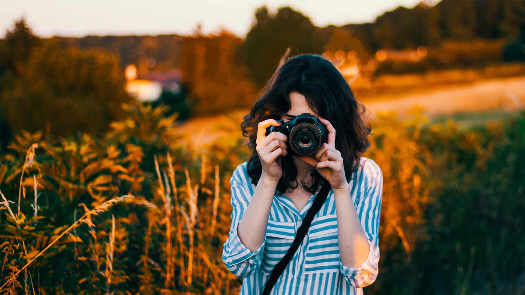 a photographer standing in a field, pointing a camera at the viewer