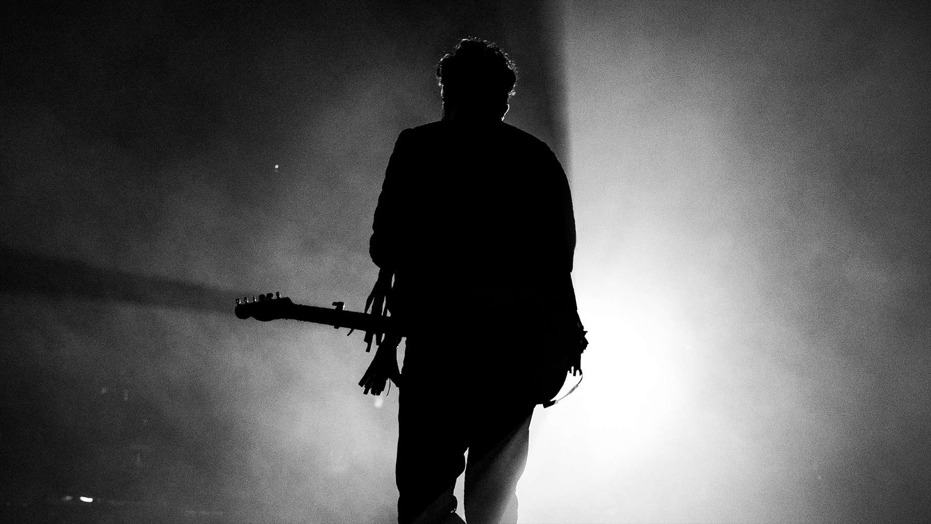 A musician holding a guitar in front of a spotlight