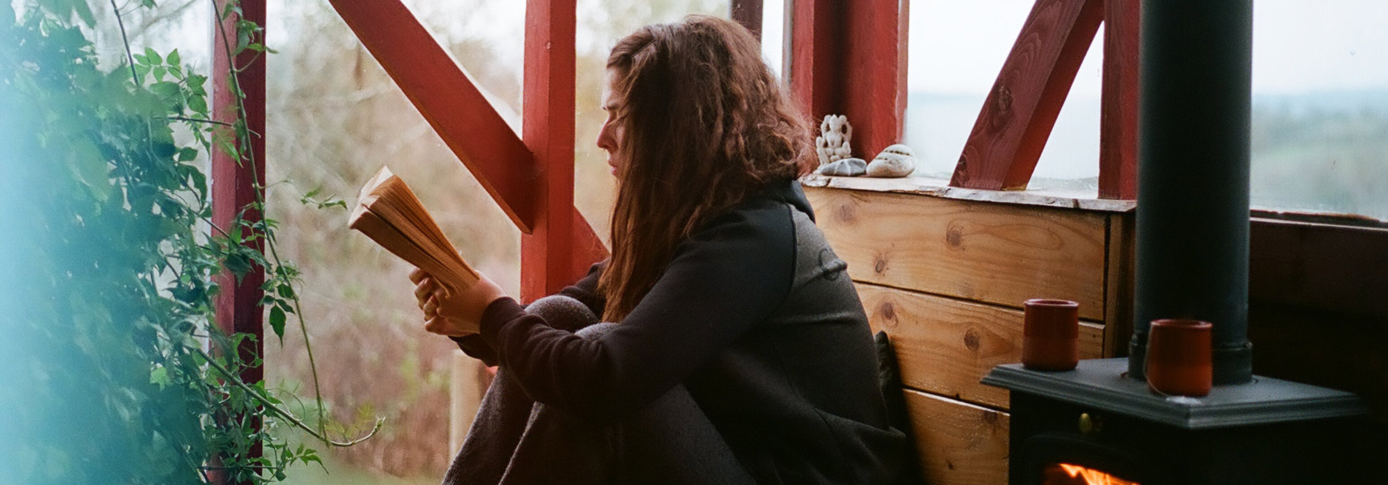 a teen reading a book in a cabin by a fire