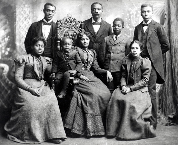 Group of black men women and children sitting for a portrait in fancy dress