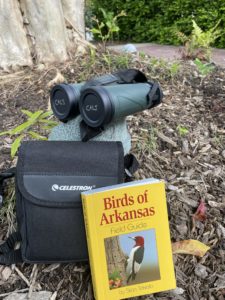 photo of the bird watching kit sitting outside, includes a book titled "Birds of Arkansas", a set of binoculars and case.